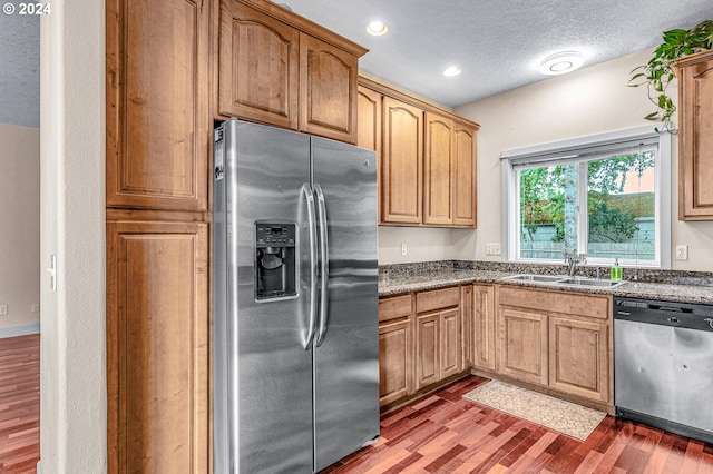 kitchen with dark stone counters, sink, stainless steel appliances, dark hardwood / wood-style floors, and a textured ceiling