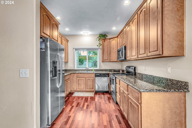 kitchen featuring dark hardwood / wood-style floors, sink, dark stone counters, appliances with stainless steel finishes, and a textured ceiling