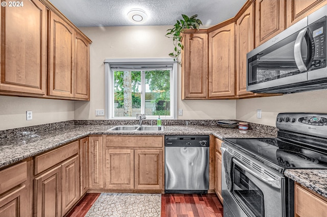 kitchen featuring stainless steel appliances, dark wood-type flooring, sink, dark stone counters, and a textured ceiling