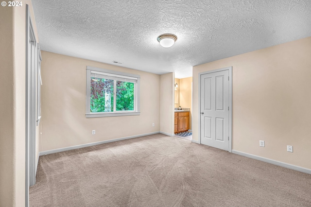 unfurnished bedroom featuring light colored carpet, a textured ceiling, and ensuite bathroom