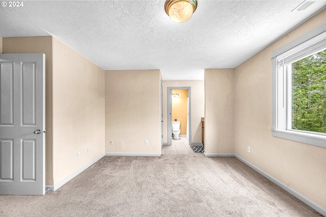 unfurnished bedroom with ensuite bathroom, multiple windows, light carpet, and a textured ceiling