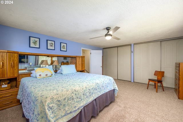 bedroom with light carpet, two closets, a textured ceiling, and ceiling fan