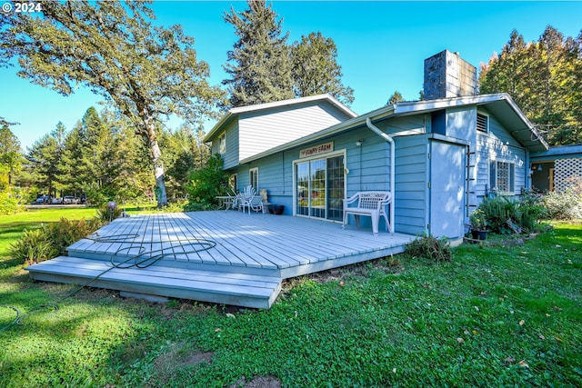 back of property featuring a chimney, a lawn, and a wooden deck