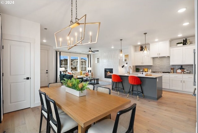 dining area with a large fireplace, light hardwood / wood-style floors, and ceiling fan with notable chandelier