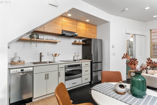 kitchen with appliances with stainless steel finishes, sink, white cabinetry, range hood, and tasteful backsplash