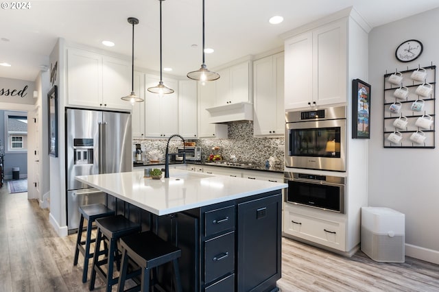 kitchen with white cabinetry, stainless steel appliances, light hardwood / wood-style floors, decorative light fixtures, and custom range hood