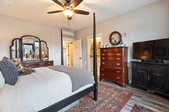 bedroom with a wall unit AC, ceiling fan, ensuite bathroom, and wood-type flooring