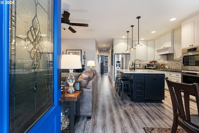 kitchen with white cabinets, wood-type flooring, a center island with sink, and hanging light fixtures