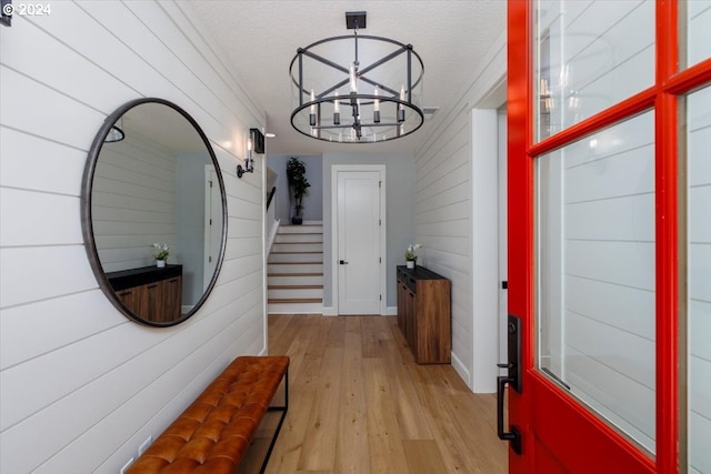 interior space featuring light wood-type flooring, a textured ceiling, a chandelier, and wooden walls