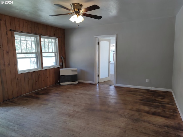 spare room featuring heating unit, wooden walls, ceiling fan, and dark wood-type flooring