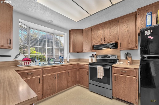 kitchen with stainless steel electric stove, exhaust hood, a textured ceiling, black refrigerator, and sink