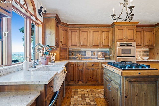 kitchen with light stone counters, decorative backsplash, appliances with stainless steel finishes, a notable chandelier, and brown cabinets