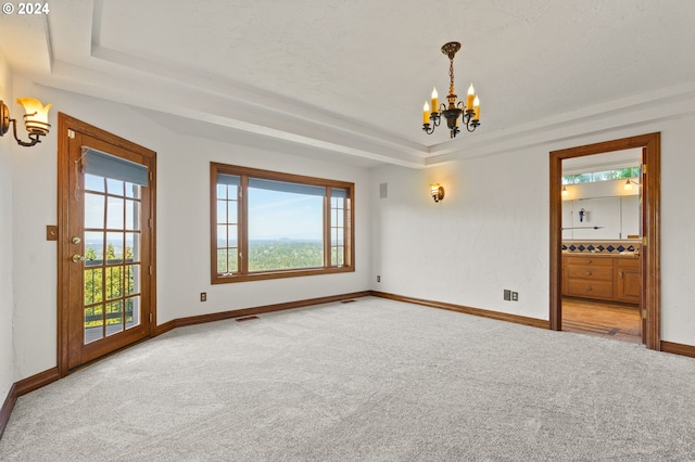 empty room featuring visible vents, baseboards, a tray ceiling, carpet floors, and a notable chandelier