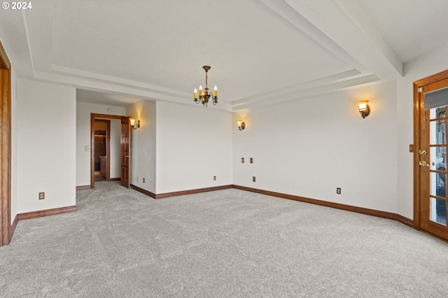 carpeted spare room featuring an inviting chandelier, a raised ceiling, and baseboards