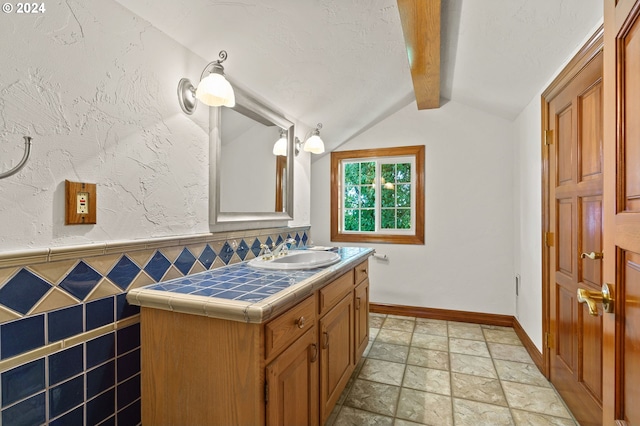 bathroom featuring vanity, vaulted ceiling with beams, stone finish flooring, and baseboards