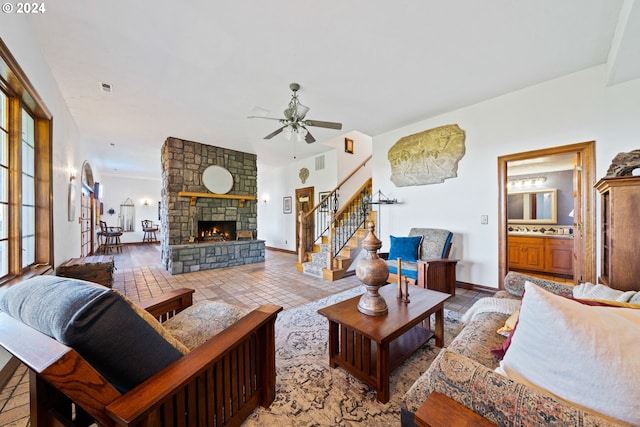 living area featuring stairway, baseboards, visible vents, a fireplace, and ceiling fan