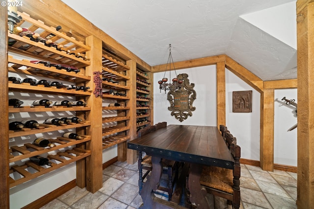 wine room with stone tile flooring, baseboards, a textured ceiling, and lofted ceiling