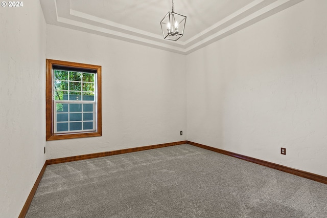 spare room featuring an inviting chandelier, a tray ceiling, carpet, and baseboards