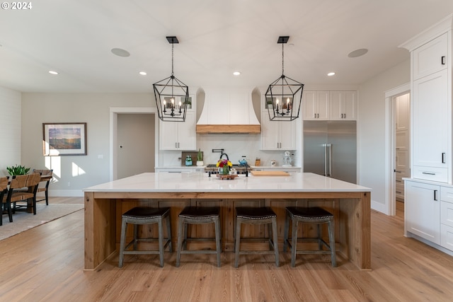 kitchen featuring white cabinetry, a large island, stainless steel built in fridge, a breakfast bar, and custom exhaust hood