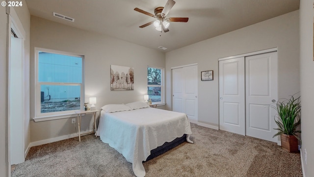 bedroom with light carpet, ceiling fan, and two closets