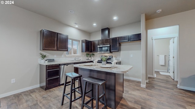 kitchen featuring stainless steel appliances, a kitchen island, dark brown cabinetry, a breakfast bar, and light hardwood / wood-style flooring