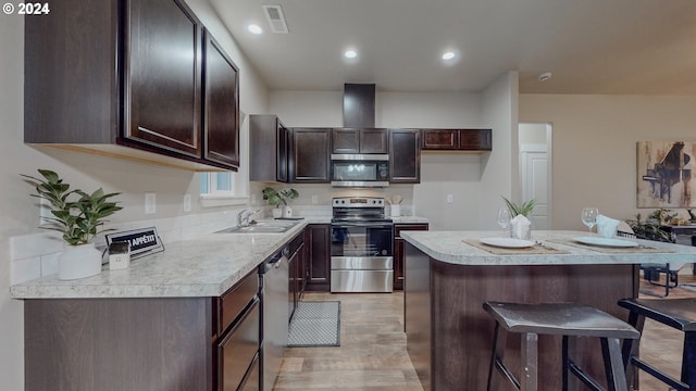 kitchen with stainless steel appliances, a kitchen island, a kitchen bar, sink, and light hardwood / wood-style flooring