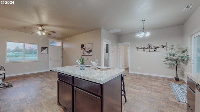 kitchen featuring ceiling fan with notable chandelier, decorative light fixtures, dark brown cabinets, light hardwood / wood-style flooring, and a center island