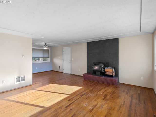 unfurnished living room with a textured ceiling, hardwood / wood-style flooring, a wood stove, and ceiling fan