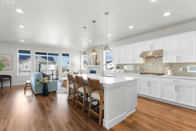 kitchen featuring stainless steel gas cooktop, sink, hanging light fixtures, a kitchen island with sink, and white cabinets