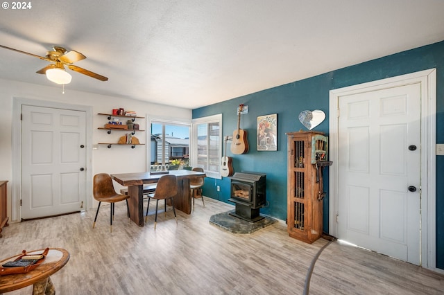 dining room featuring light wood-type flooring, a wood stove, and ceiling fan