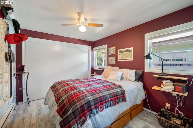 bedroom featuring baseboard heating, ceiling fan, wood-type flooring, an AC wall unit, and a closet