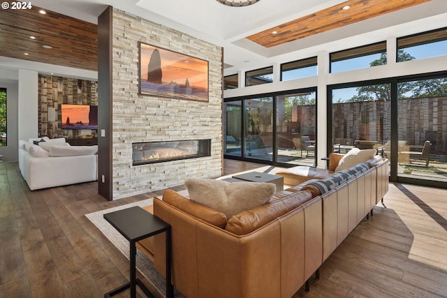 living room with a high ceiling, a stone fireplace, wood-type flooring, and a raised ceiling