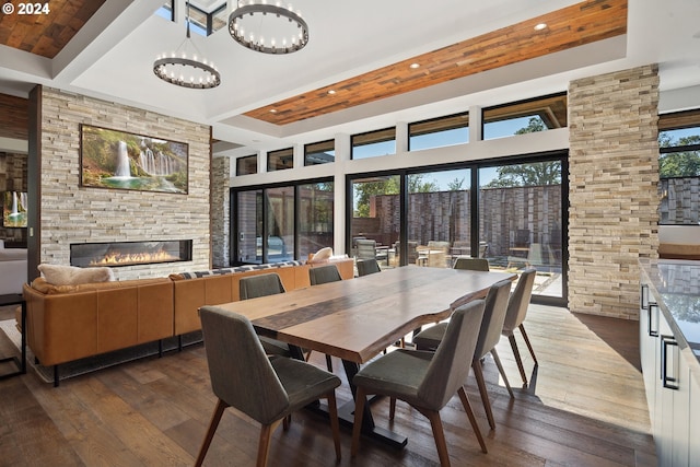 dining space with dark wood-type flooring, an inviting chandelier, a towering ceiling, and a stone fireplace