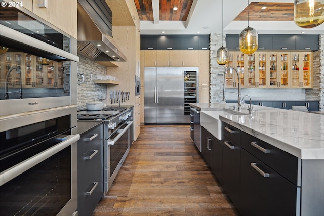 kitchen featuring a kitchen island with sink, wall chimney exhaust hood, hanging light fixtures, sink, and dark hardwood / wood-style flooring