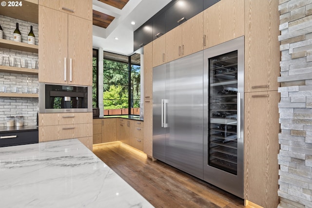 kitchen featuring oven, light stone countertops, light brown cabinetry, and dark hardwood / wood-style flooring