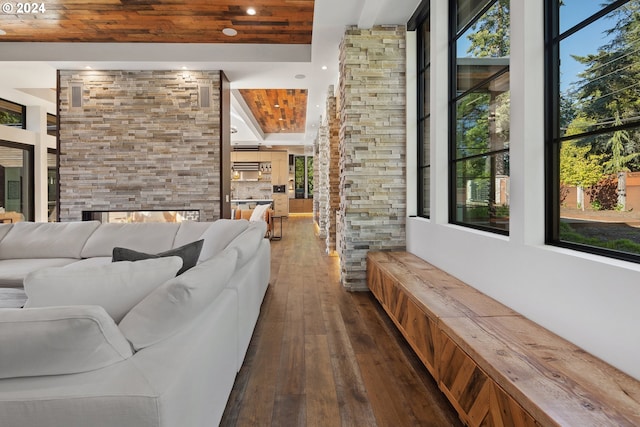 living room with dark wood-type flooring, a stone fireplace, wooden ceiling, and beamed ceiling