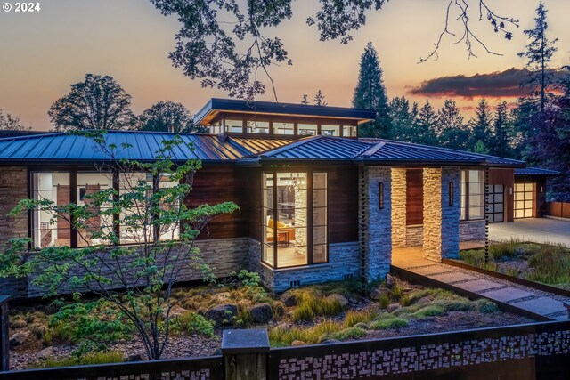 view of front facade featuring concrete driveway, a standing seam roof, stone siding, and metal roof