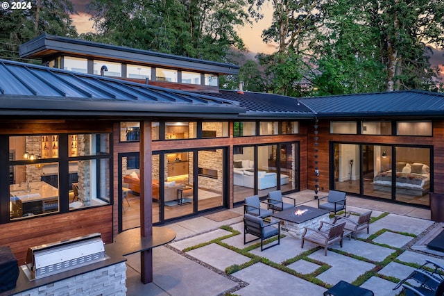 back of property at dusk featuring a patio area, an outdoor living space with a fire pit, metal roof, and a standing seam roof
