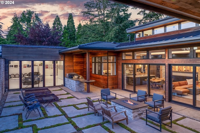 back of house at dusk with an outdoor fire pit, a patio, an outdoor kitchen, and metal roof