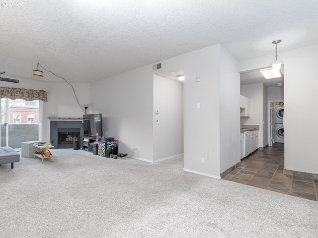 living room with stacked washing maching and dryer, a textured ceiling, and dark colored carpet