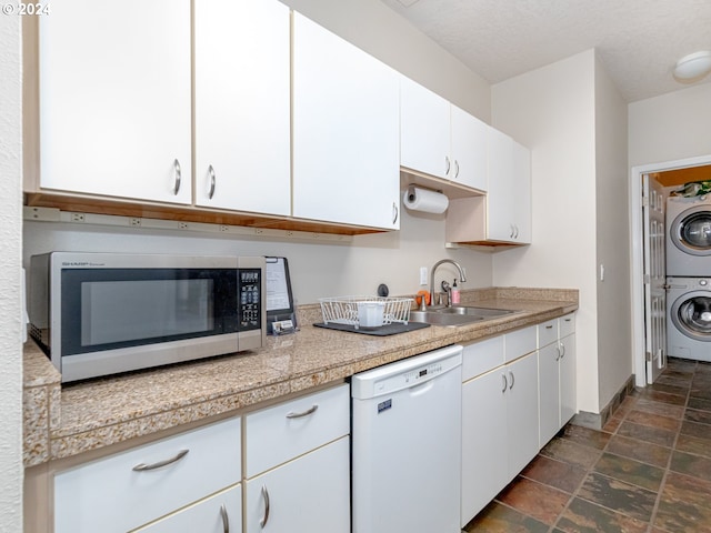 kitchen with white dishwasher, white cabinets, stacked washing maching and dryer, and sink