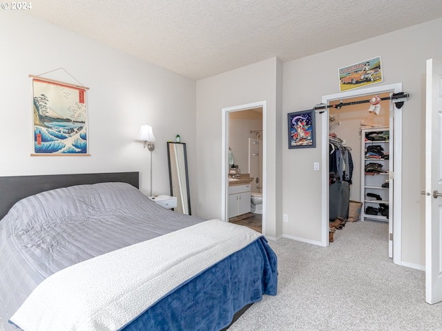 bedroom with carpet flooring, connected bathroom, a spacious closet, a textured ceiling, and a closet