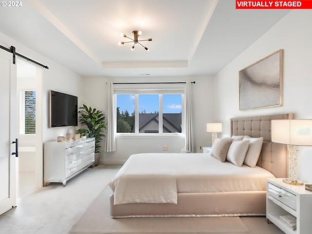 bedroom with a barn door, multiple windows, a tray ceiling, and an inviting chandelier