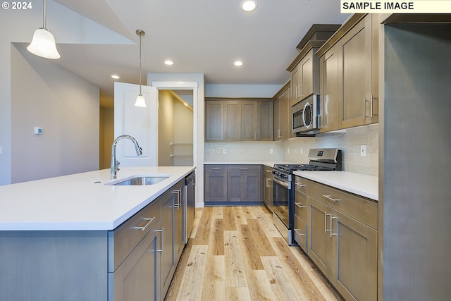 kitchen featuring sink, appliances with stainless steel finishes, an island with sink, pendant lighting, and light hardwood / wood-style floors