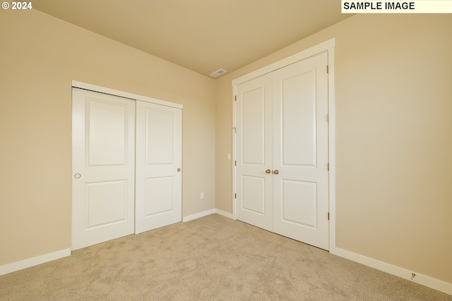 unfurnished bedroom with light colored carpet and a closet