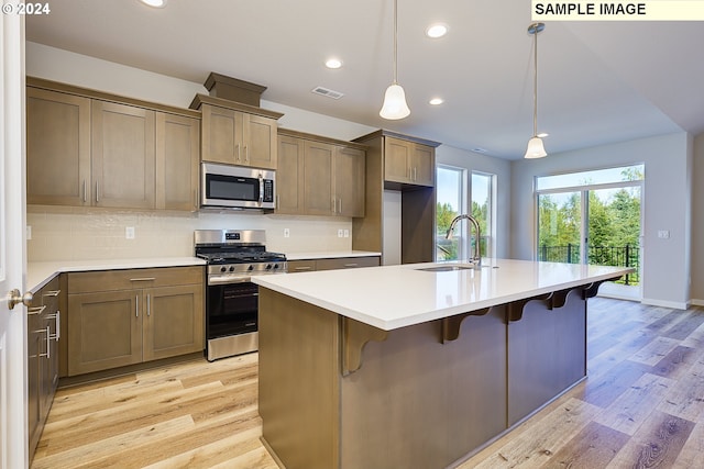 kitchen with sink, appliances with stainless steel finishes, a kitchen island with sink, hanging light fixtures, and a kitchen breakfast bar