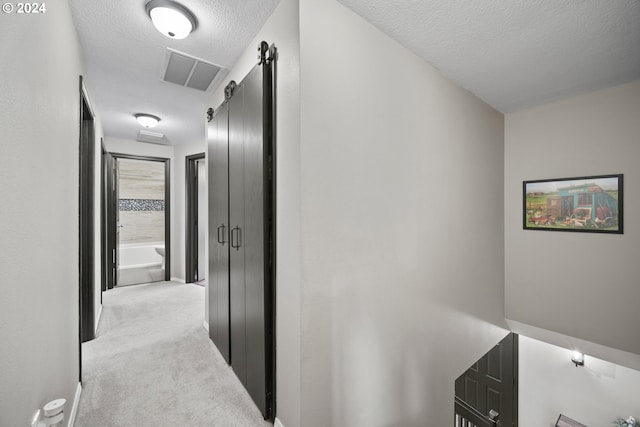 corridor with a textured ceiling, light carpet, and a barn door