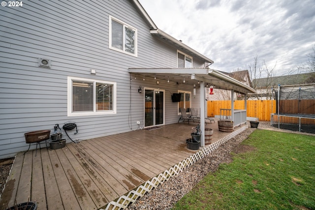 back of house featuring an outdoor fire pit, a deck, a yard, and a trampoline