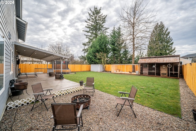 view of yard featuring a deck, a fire pit, an outbuilding, and a trampoline