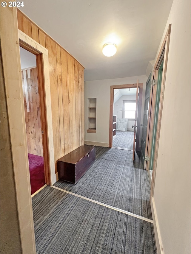 hallway featuring wood walls and dark colored carpet